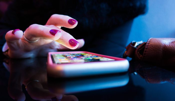 Woman’s-hand-using-smartphone-on-flat-surface