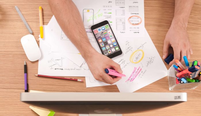 Desk-photographed-from-above-with-hands-writing-on-papers-in-front-of-a-computer