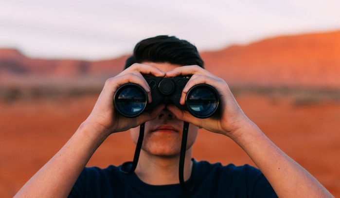 Man-looking-through-binoculars-in red-landscape