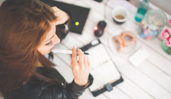Woman-at-desk-thinking-with-pen-in-mouth