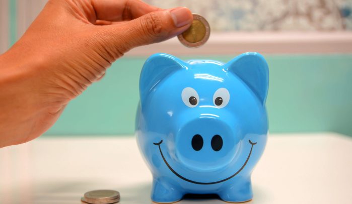 Hand-putting-coin-into-a-smiling- blue-piggy-bank