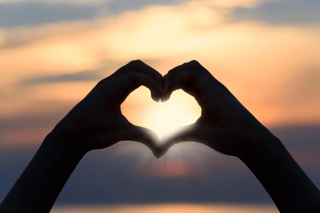 Hands forming heart against sunset background