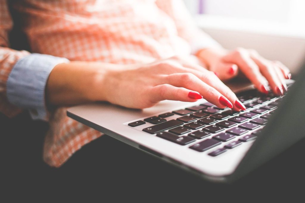 Hands with red nails typing on laptop