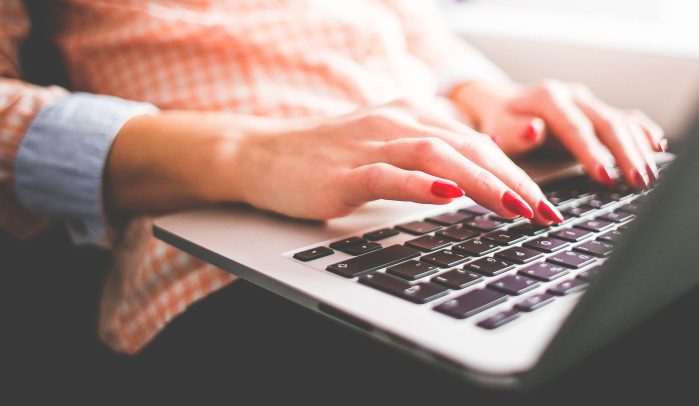 Hands with red nails typing on laptop