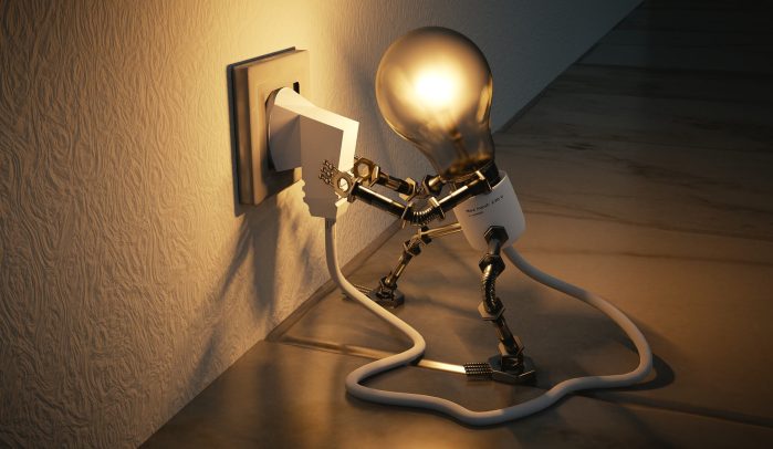 Lit lightbulb man plugging himself into an electric wall socket