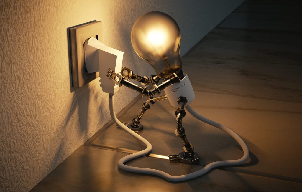 Lit lightbulb man plugging himself into an electric wall socket