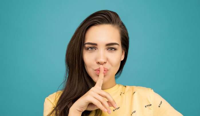 Woman-with-finger-over-lips-on-blue-background