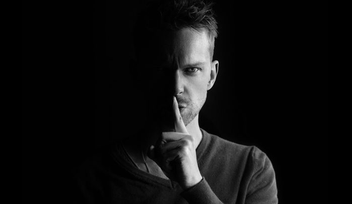 Monochorme-image-of-man-in-shadows-with-finger-on-lips