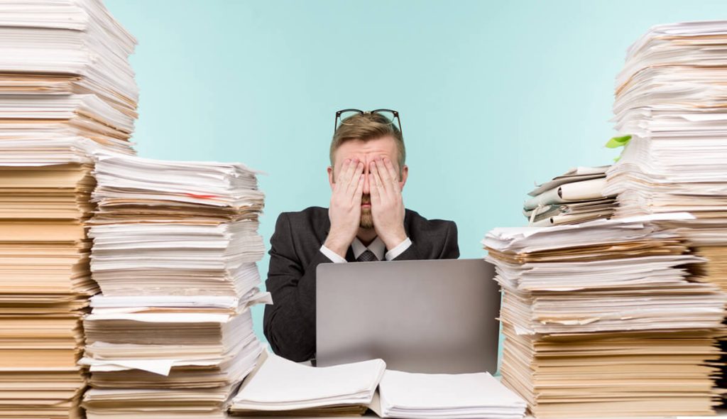 Man-with-hands-over-his-eyes-surrounded-by-piles-of-paper