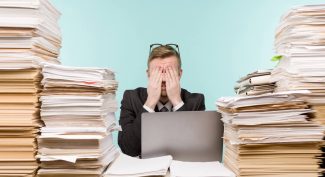 Man-with-hands-over-his-eyes-surrounded-by-piles-of-paper