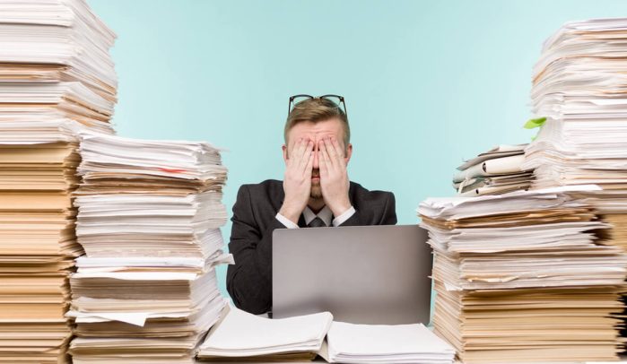 Man-with-hands-over-his-eyes-surrounded-by-piles-of-paper